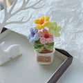 Single pink crochet bloom with green leaves in a cream pot.