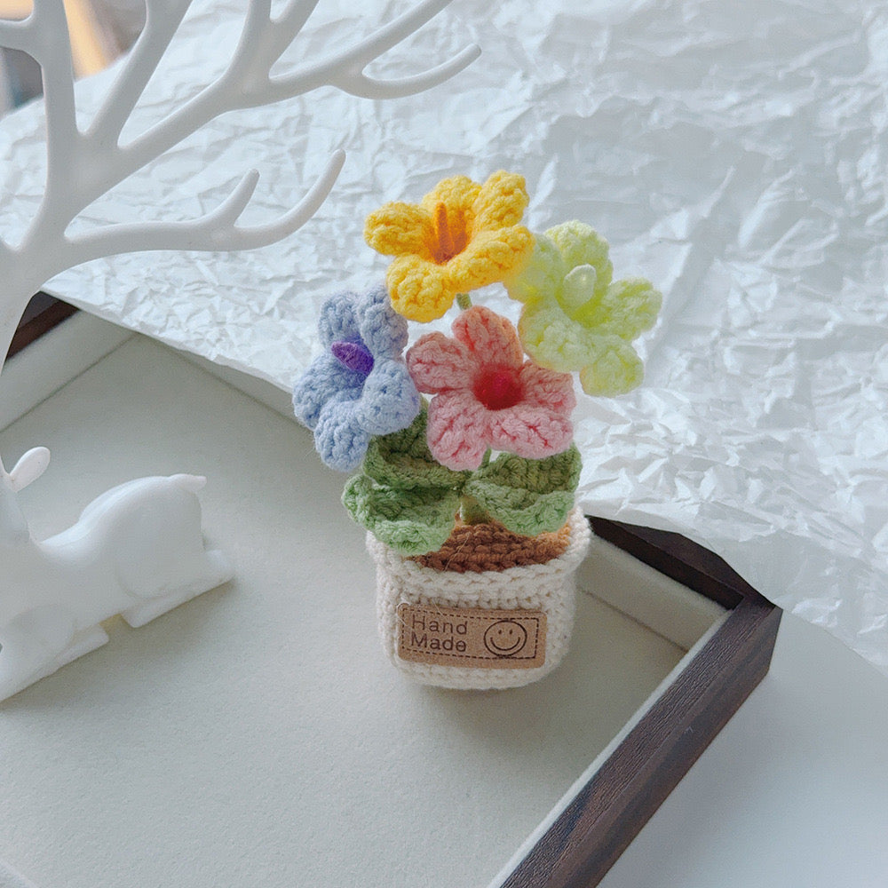 Single pink crochet bloom with green leaves in a cream pot.